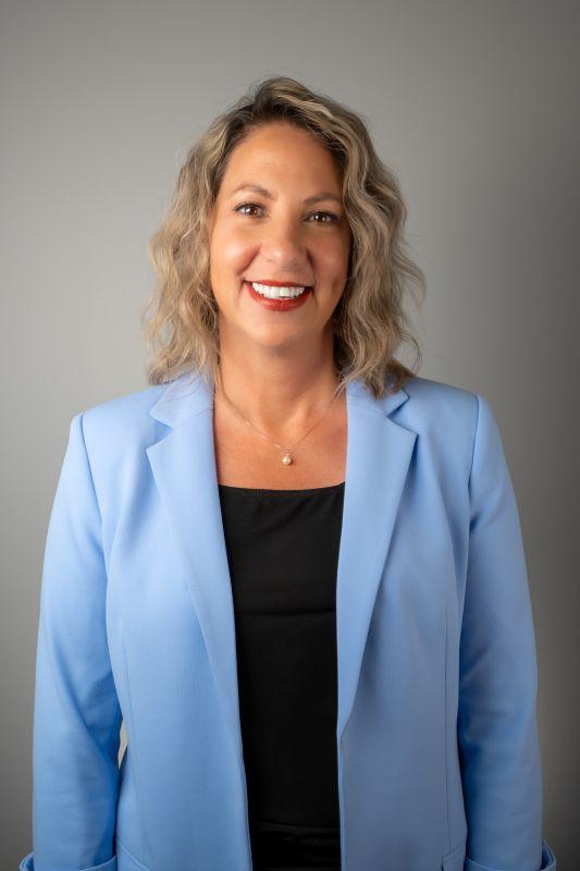 Headshot of Alison, a middle-aged Caucasian woman with chin-length blonde hair and dark eyes. She is wearing a black shirt with a pale blue blazer.
